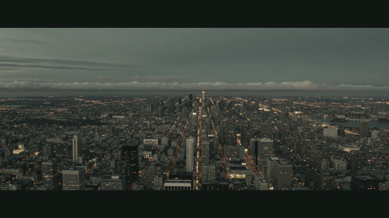 A city at dusk, one long avenue of light running to the horizon. The opening frame of the series trailer.